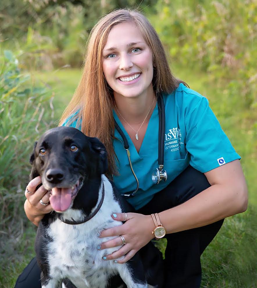 Caitlyn Rize squats smiling next to a black dog with a white stomach sticking out its tongue.