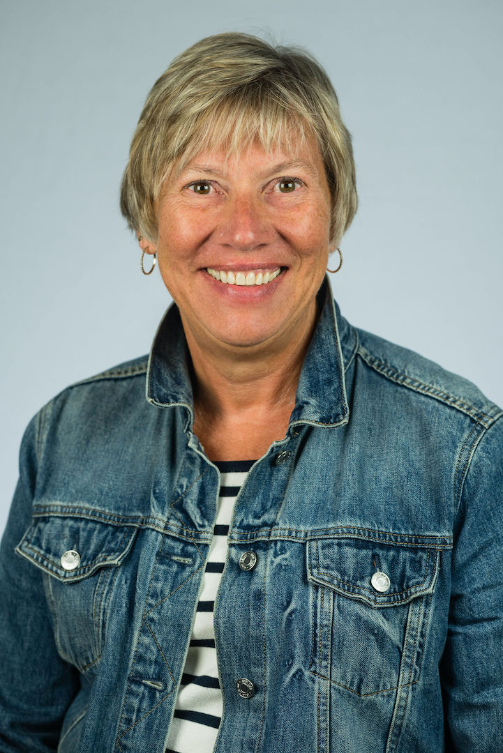 Lisa Hubinger smiles at the camera for her professional headshot. She is wearing a blue jean jacket and a black and white striped shirt. 
