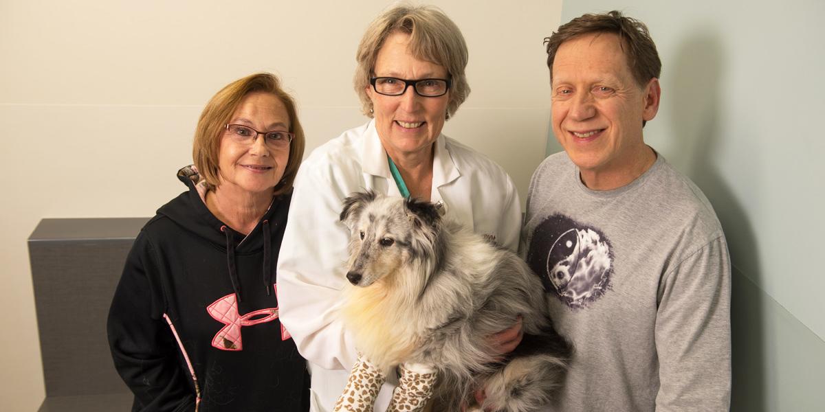 Dr. Kramek poses while holding a dog patient while standing next the owners