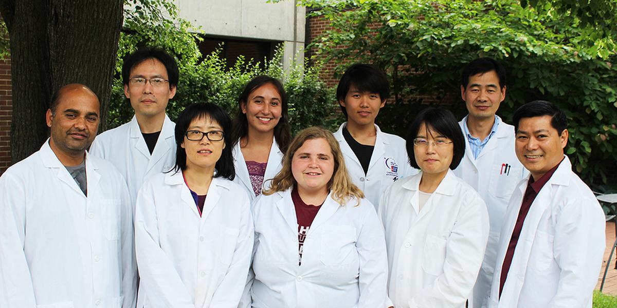 The Liang-Ly lab wears white coats outside and smiles together at the camera